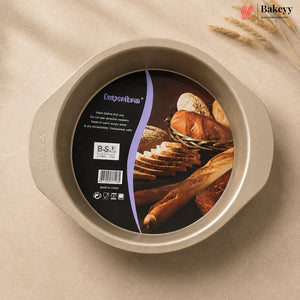 A round non-stick baking pan with side handles, shown from above on a beige fabric background with wheat stalks. The inside has a black and purple product label featuring bread imagery and the brand name 'Outperform'.