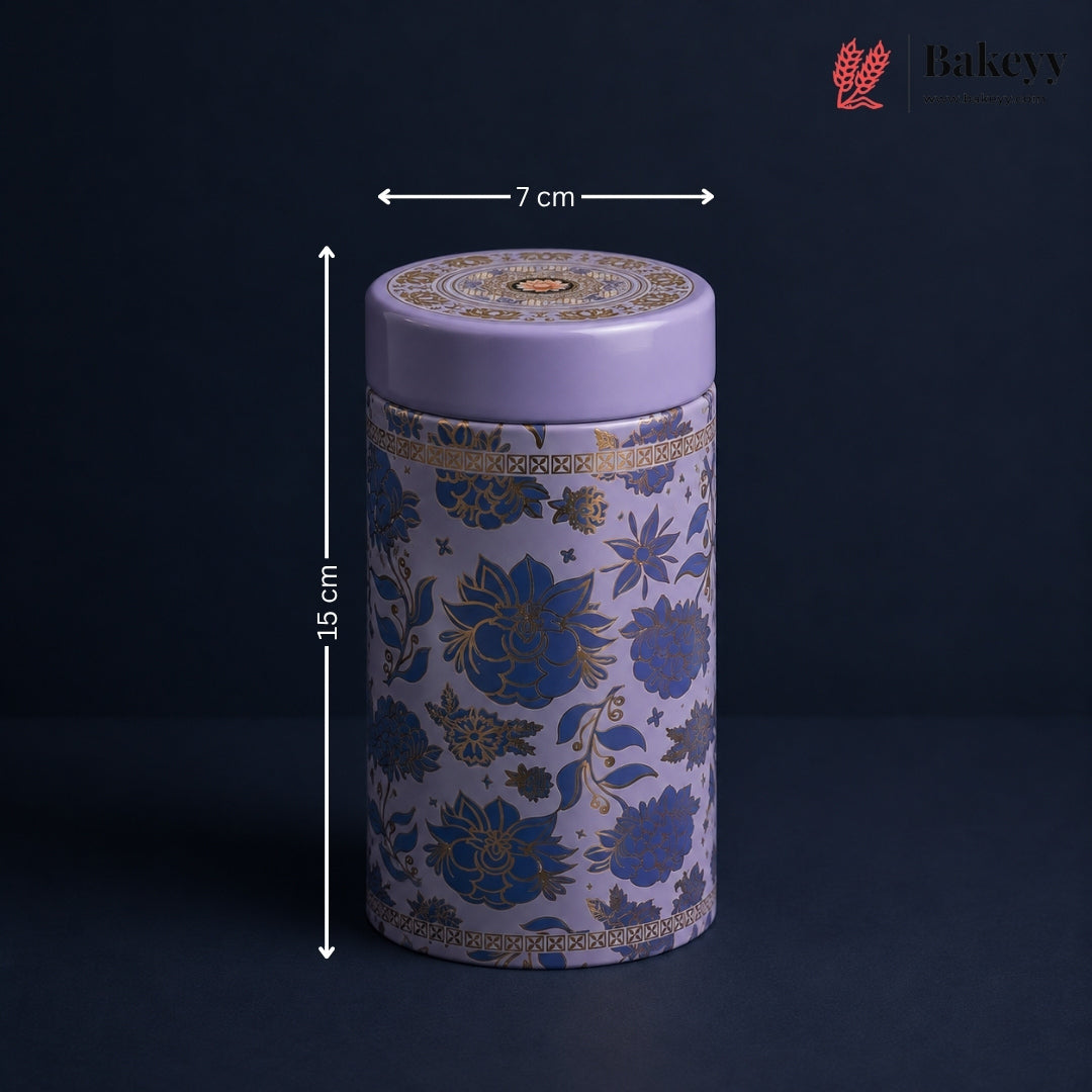 A cylindrical decorative tin with a lavender purple lid and base, decorated with blue and gold floral patterns, shown with dimension arrows indicating a height of 15 cm and a width of 7 cm. The Bakeyy logo is visible in the top right corner.