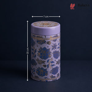 A cylindrical decorative tin with a lavender purple lid and base, decorated with blue and gold floral patterns, shown with dimension arrows indicating a height of 15 cm and a width of 7 cm. The Bakeyy logo is visible in the top right corner.