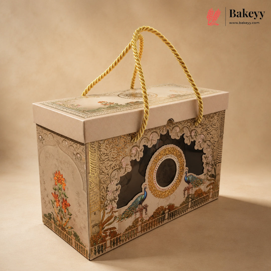 An ornate rectangular gift box with a cream-colored lid and sides, decorated with intricate gold, blue, and orange floral and bird illustrations. The box features a central cutout window and is equipped with a thick gold rope handle, set against a warm beige background.