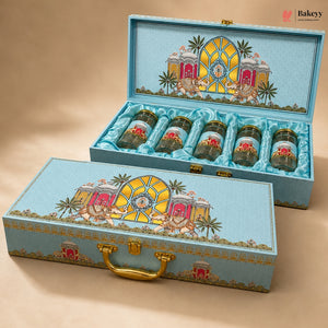 A decorative turquoise gift box set with five small jars arranged inside an open box and one matching closed box in front. The boxes feature a colorful architectural illustration with pink carriages, palm trees, and gold details, and the jars have gold lids.