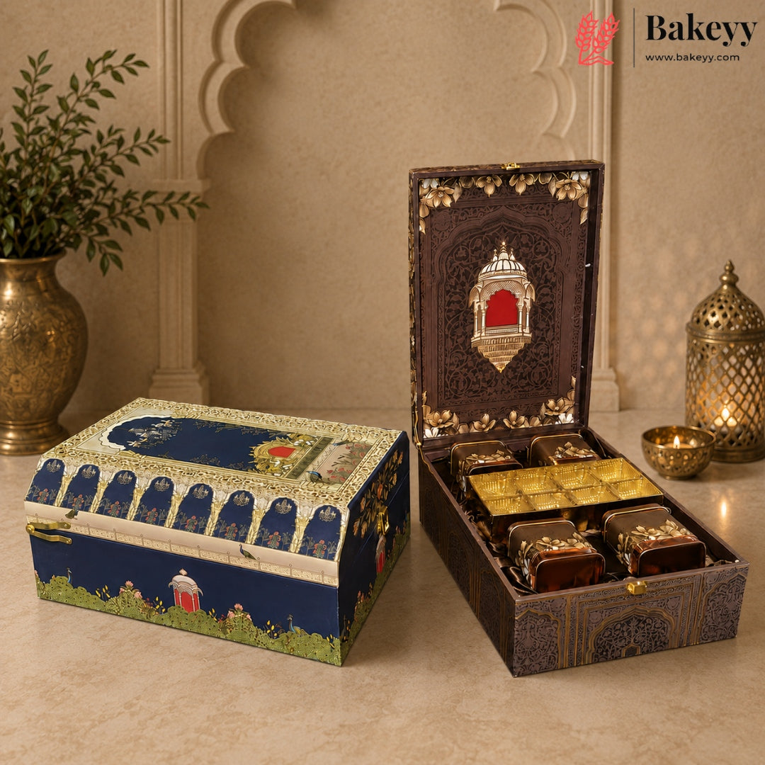 An ornate gift set displayed in two decorative boxes on a beige stone surface. One closed box features a blue and gold architectural illustration with green grass at the bottom.