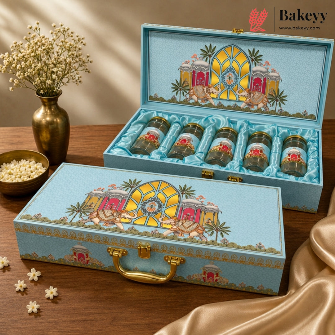 A decorative light blue gift box set with gold hardware, shown open and closed on a wooden table. The boxes feature an illustrated tropical pavilion design on the lid and contain small glass jars with red floral labels.