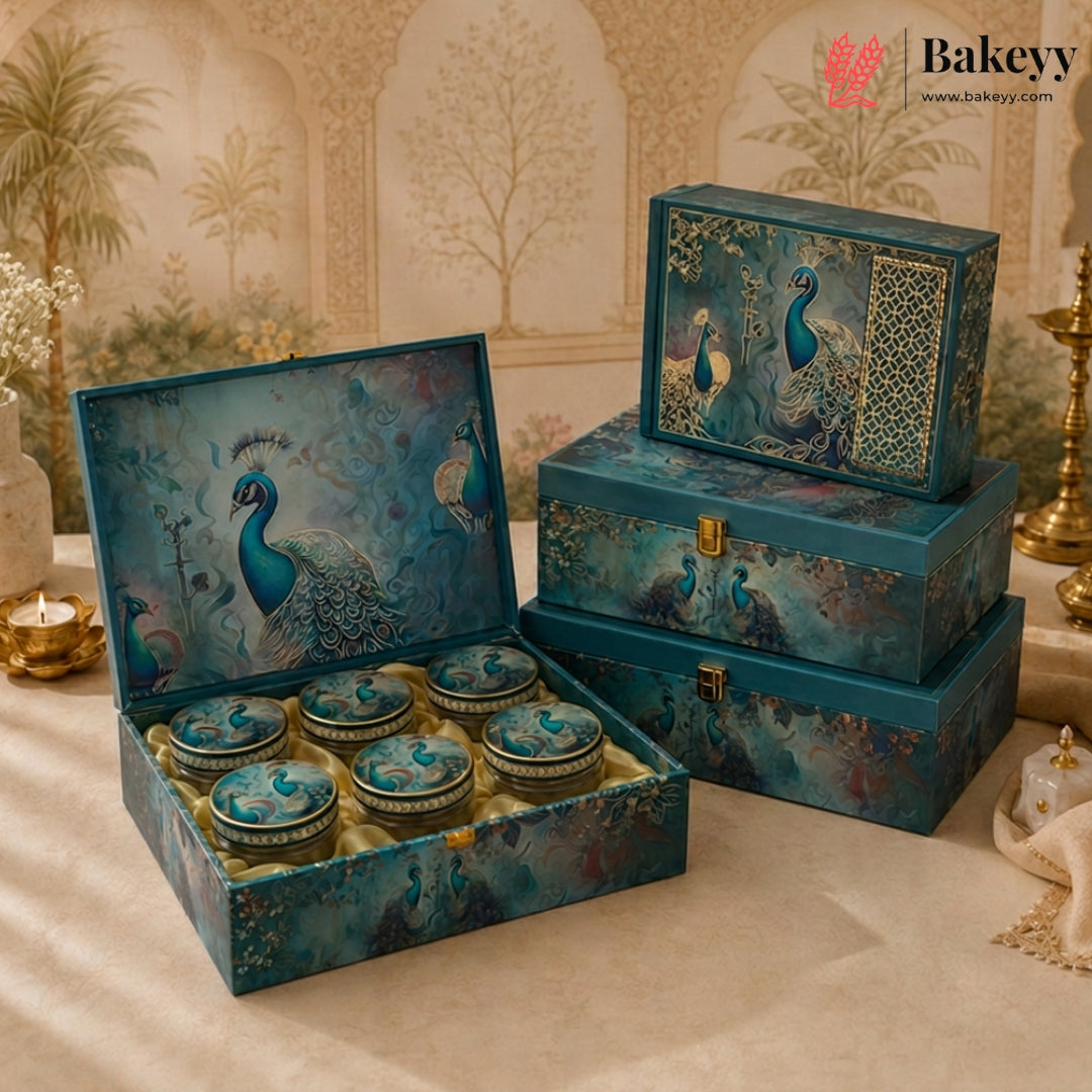 A decorative gift set featuring a large open box with six small round tins and two closed storage boxes, all decorated with a blue peacock illustration. The set is displayed on a draped beige fabric surface with ornate decorative props in the background.