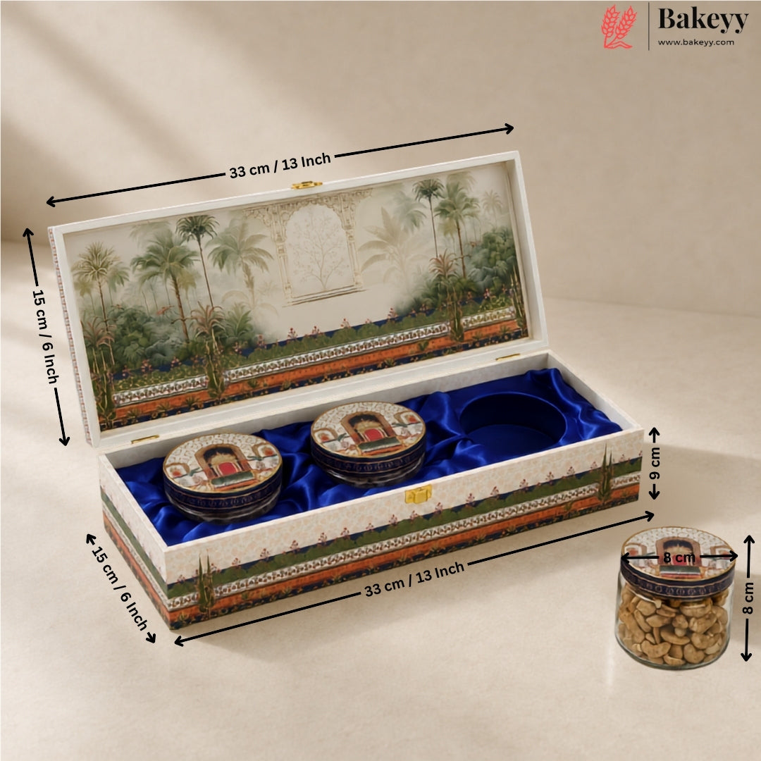 An open decorative gift box for cookies or sweets, shown with dimension arrows and labels. The box has a white exterior with a painted tropical garden scene on the lid and base, blue velvet interior lining, and two round cookie jars placed inside.