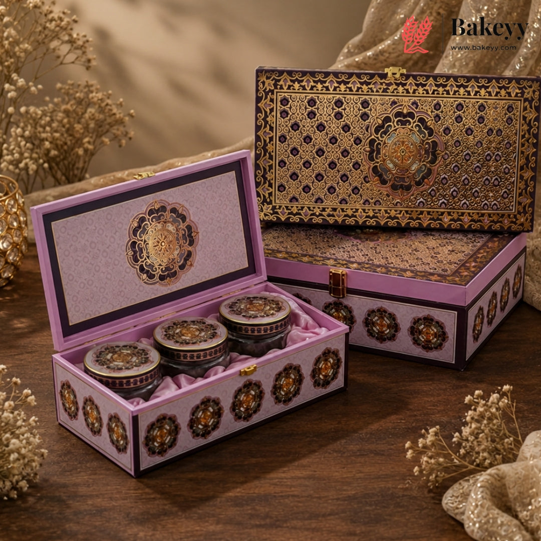 An ornate pink and gold gift box set displayed on a wooden surface, with one open box holding three small round containers and one closed box behind it. The boxes feature intricate gold floral patterns and a pink velvet interior.