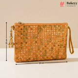 An orange sequined clutch bag with a wrist strap and gold-toned tassel zipper pull, shown with dimension lines indicating 20 cm width and 10 cm height on a beige background. Bakeyy branding is visible in the top right.