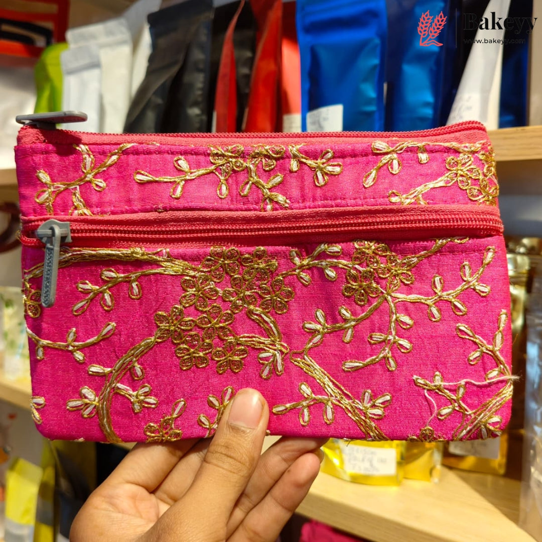 A bright pink zippered pouch with gold floral embroidery, held by a hand in front of a store background.