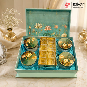 A gourmet tea gift set in a decorative mint green box with a floral lotus design on the inside lid. The set includes four round metal tea tins with matching floral lids and a central gold-toned tray, arranged on a marble surface with decorative props.