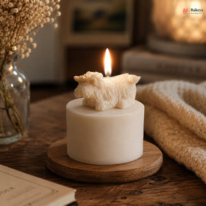 Small white candle with a sheep figurine on top, lit on a wooden coaster.