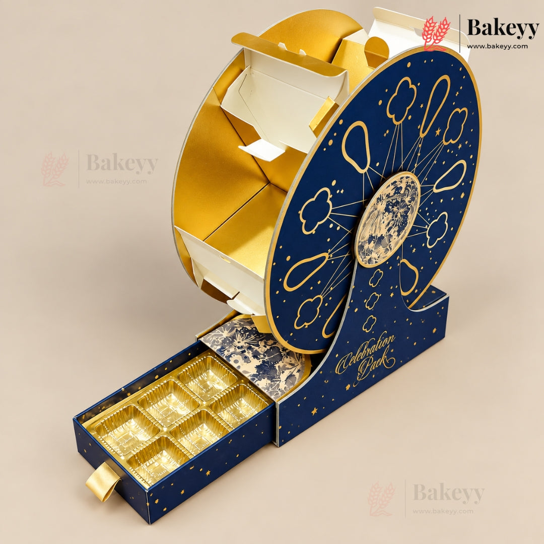 A decorative round pastry or chocolate gift box with a sliding drawer, shown on a plain beige background. The top half is metallic gold with white interior compartments, and the bottom half is dark blue with gold stars and cloud-like line art.
