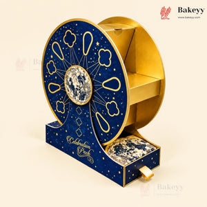 A decorative gift box set for 'Celebration Puck' featuring a large circular wheel design in navy blue and gold with a central moon emblem, alongside a matching drawer containing marbled sweets, all on a light beige background.
