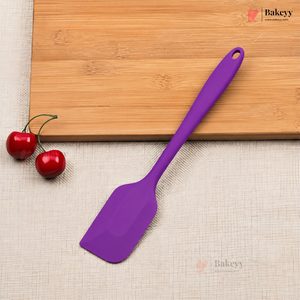 Purple spatula on a beige surface with a wooden cutting board and red cherries in the background.