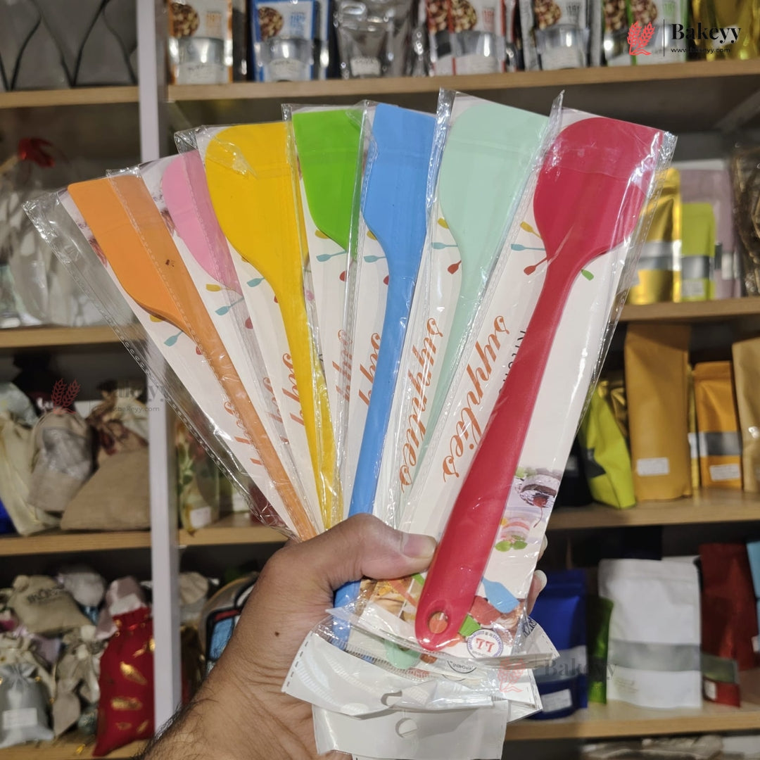 Set of colorful spatulas in packaging held by a person with a store shelf in the background