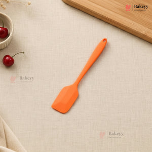 Orange spatula on a beige surface with cherries and a wooden board in the background, featuring the Bakeyy brand.