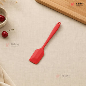 Red spatula on a beige surface with cherries and a wooden board, featuring the Bakeyy brand.