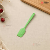 Green spatula on a beige surface with cherries and a wooden board.