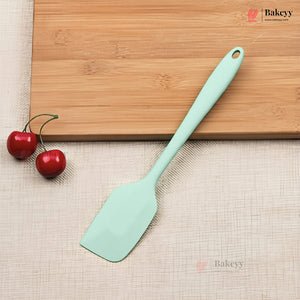 Light blue spatula on a wooden cutting board with two red cherries, on a beige textured surface.