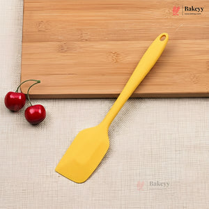 Yellow spatula on a wooden cutting board with two red cherries, on a beige surface with 'Bakeyy' branding.