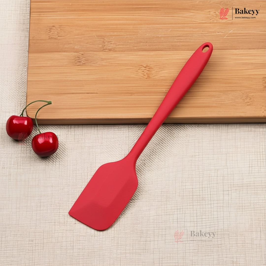 Red spatula on a wooden cutting board with cherries, on a beige surface with 'Bakeyy' branding.
