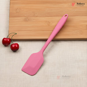 Pink spatula on a wooden cutting board with cherries, on a beige surface with 'Bakeyy' branding.