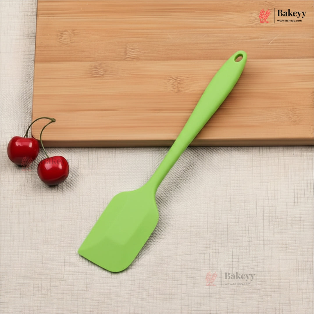 Green spatula on a wooden cutting board with cherries, on a beige surface with 'Bakeyy' branding.