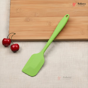 Green spatula on a wooden cutting board with cherries, on a beige surface with 'Bakeyy' branding.