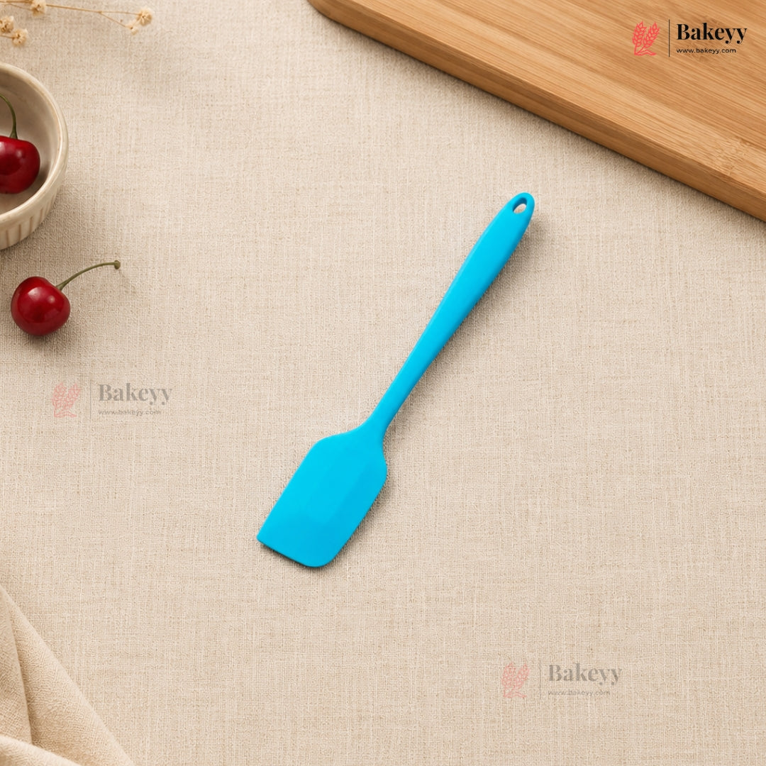 Blue spatula on a beige surface with cherries and a wooden board, featuring the Bakeyy brand.