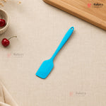 Blue spatula on a beige surface with cherries and a wooden board, featuring the Bakeyy brand.