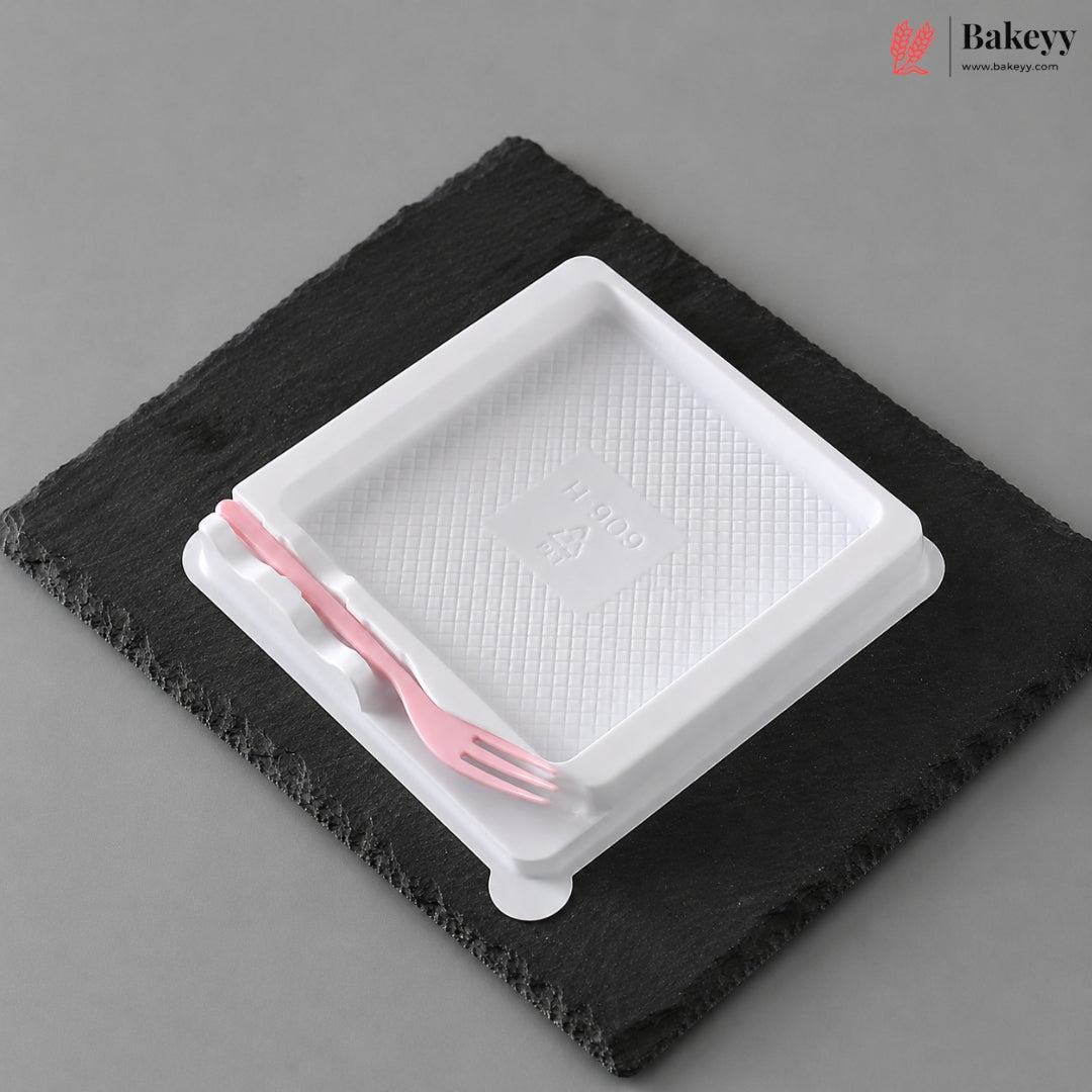 A white plastic tray with a textured interior and a small pink plastic fork resting inside, placed on a dark charcoal slate coaster against a neutral gray background.