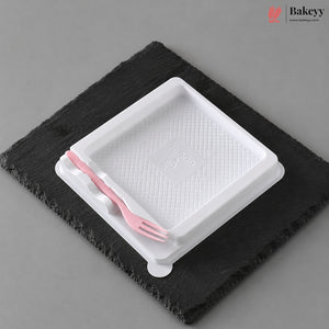A white plastic tray with a textured interior and a small pink plastic fork resting inside, placed on a dark charcoal slate coaster against a neutral gray background.