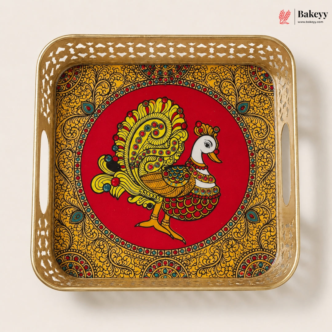 A square decorative tray with cutout handles, featuring a red center with a stylized peacock illustration and an ornate gold paisley border, photographed on a plain light background. The Bakeyy logo appears in the top right corner.