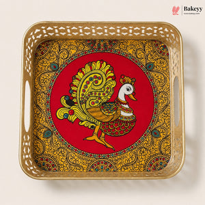 A square decorative tray with cutout handles, featuring a red center with a stylized peacock illustration and an ornate gold paisley border, photographed on a plain light background. The Bakeyy logo appears in the top right corner.