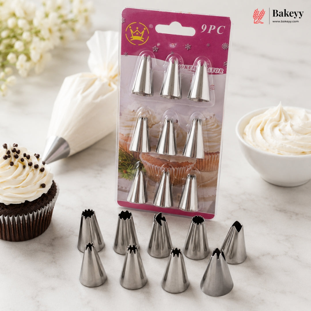A 9-piece set of stainless steel icing tip nozzles displayed on a marble surface, with some tips arranged in front of their pink retail packaging. A piping bag with white icing, a decorated cupcake, and a bowl of icing are styled around the product.