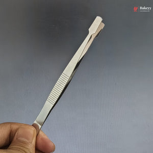 Metallic tweezer held by a hand against a gray background