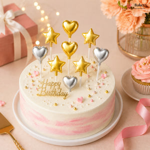 Birthday cake with pink and white frosting, gold and silver candles, and a cupcake in the background.