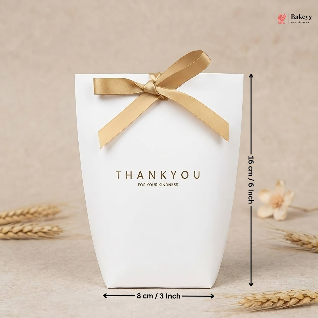 White gift box with gold ribbon and 'THANKYOU' text, placed on a beige surface with wheat stalks.