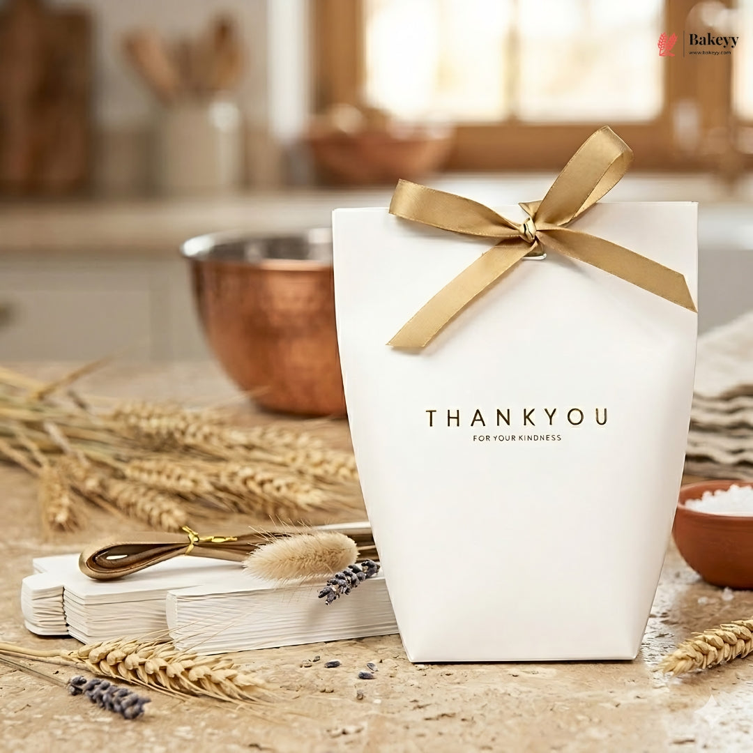 White gift box with gold ribbon and 'THANKYOU' text on a kitchen counter with baking ingredients.