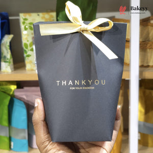 Blue gift box with a yellow ribbon held by a hand, with 'Bakeyy' branding in the background.
