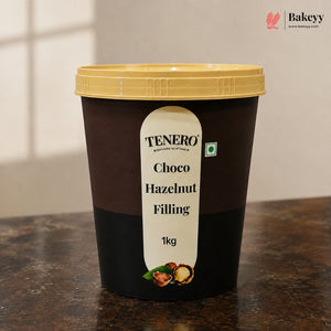 A 1kg tub of TENERO Choco Hazelnut Filling with a dark brown body, cream-colored label, and a yellow lid, sitting on a dark countertop.