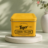 A yellow metal tin of Tiger Lemon Yellow synthetic food colour, displayed on a round white pedestal against a soft green background with a decorative vase in the distance.