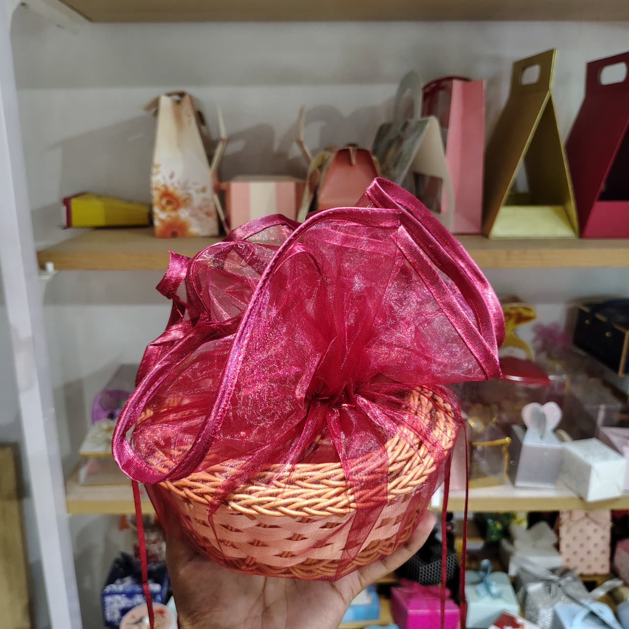 Wicker basket with a pink ribbon held in front of a shelf with various items.