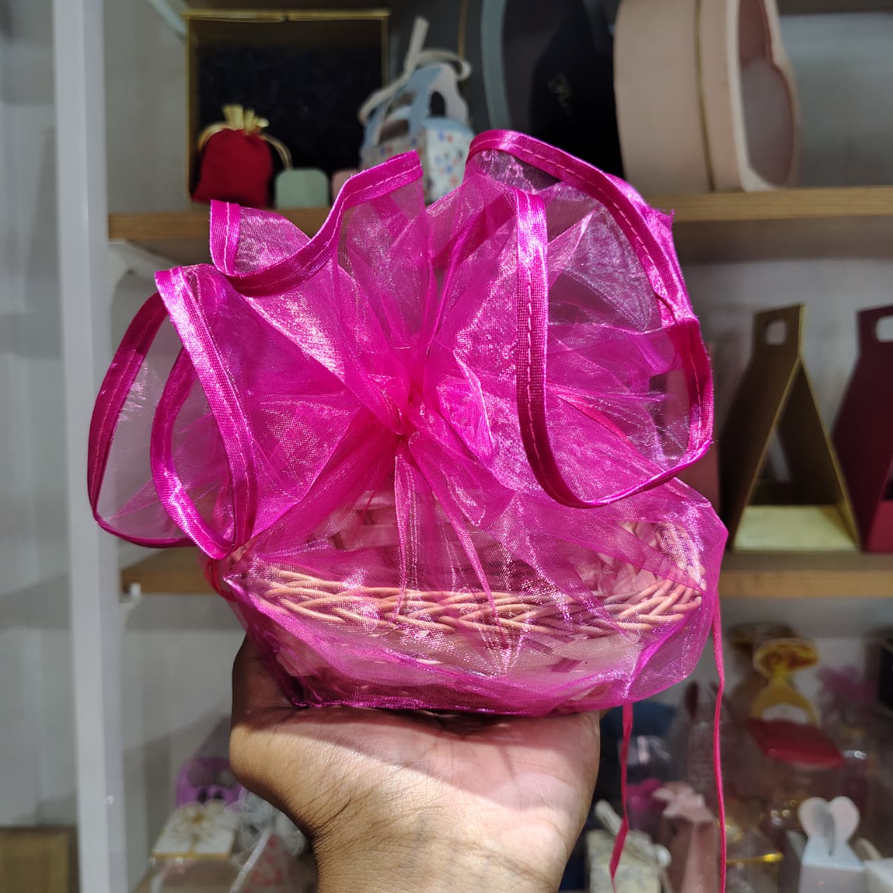 Pink gift basket with a large bow held by a hand against a blurred indoor background