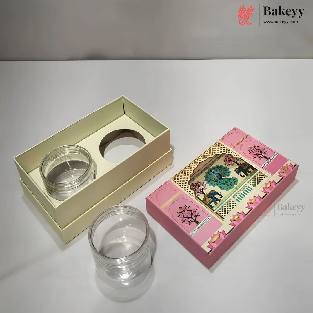 Clear glass jar with a screw-top lid shown next to its cream-colored presentation box and a pink decorative gift box with elephant artwork, on a white surface.