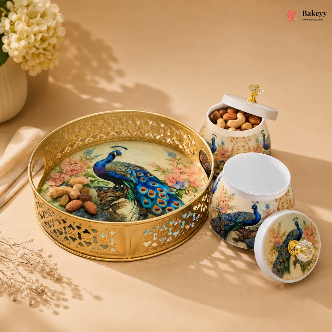 A decorative ceramic and metal baking tin set with peacock illustrations, shown on a warm beige surface with flowers in the background. The set includes a round perforated gold tray and matching jars with lids, one filled with nuts.