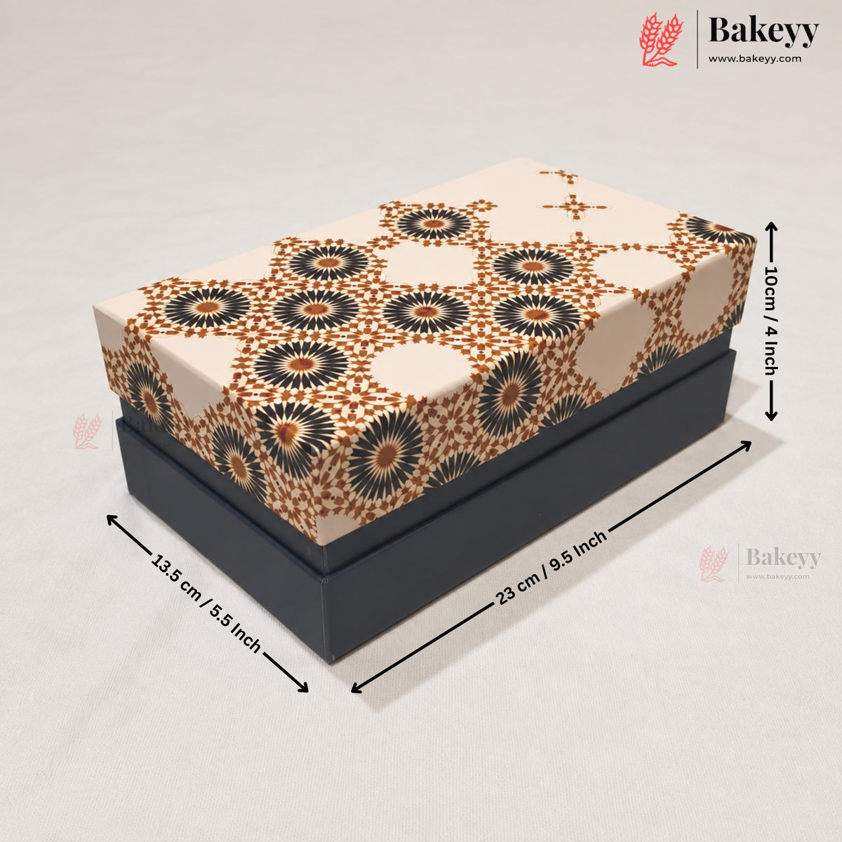 A rectangular cake or gift box with a dark charcoal base and a patterned top featuring beige, brown, and black floral motifs, shown with dimension arrows and labels indicating 23 cm by 10 cm by 13.5 cm.
