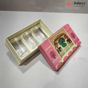 Three clear glass cups presented in a cream-colored tray inside a pink decorative gift box, with the illustrated lid placed beside it on a light gray surface.