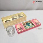 A pink and gold decorative gift box set from Bakeyy, containing three clear glass jars and a small round tin, displayed on a light gray surface with a neutral background.
