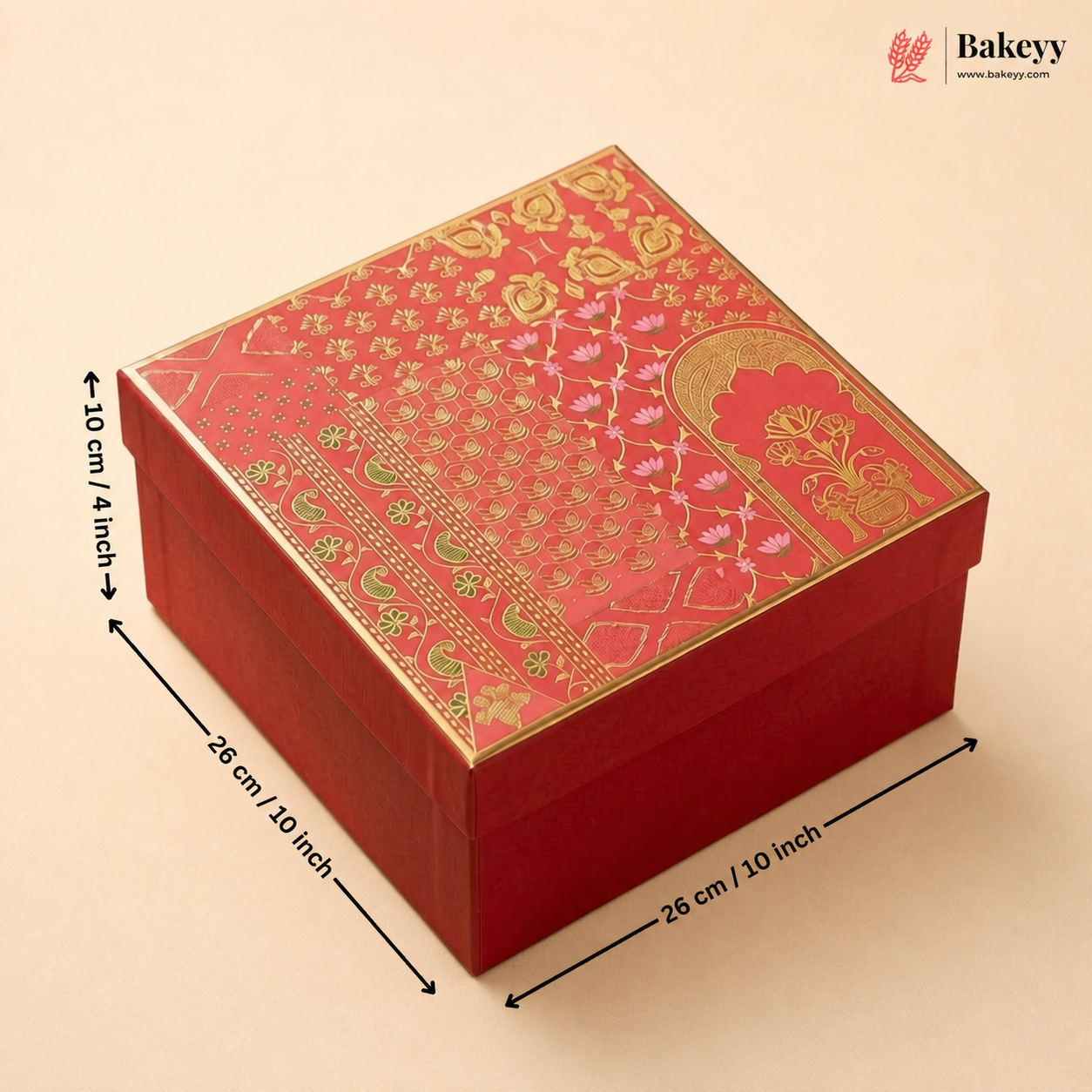 A red square gift box with ornate gold foil patterns on the lid, shown with black dimension arrows and text indicating measurements of 26 cm by 26 cm by 10 cm. The Bakeyy logo appears in the top right corner.
