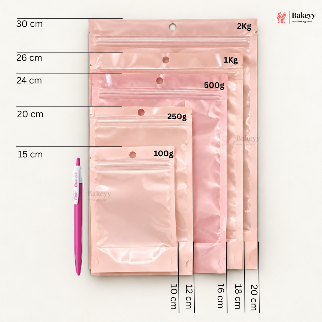 A set of translucent pink bakery bags in different sizes with printed weight labels (100g, 250g, 500g, 1Kg, 2Kg) and size measurements in centimeters, shown next to a pink pen on a white background. The Bakeey brand logo is visible in the top right.